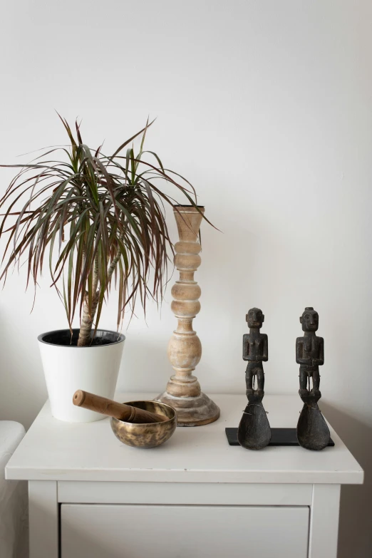 a white table with a potted plant on top of it, a statue, inspired by Diego Giacometti, unsplash, folk art, african iconography, shades of gold display naturally, detail shots, cottage decor