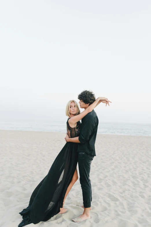 a man and woman standing on top of a sandy beach, unsplash, romanticism, black gown, dance, in front of white back drop, date