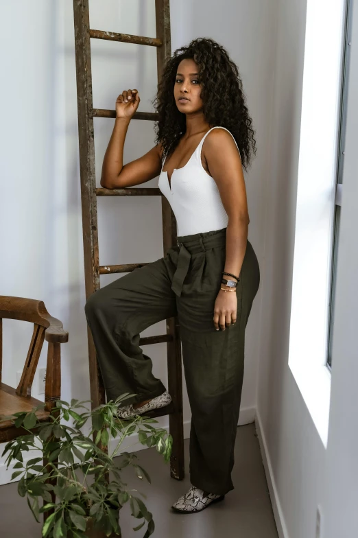 a woman standing next to a ladder in a room, inspired by Esaias Boursse, trending on pexels, olive green slacks, african american young woman, confident relaxed pose, curls