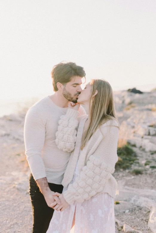 a man and woman standing next to each other on a rocky beach, pexels contest winner, romanticism, kissing together cutely, winter sun, white hue, portra 160