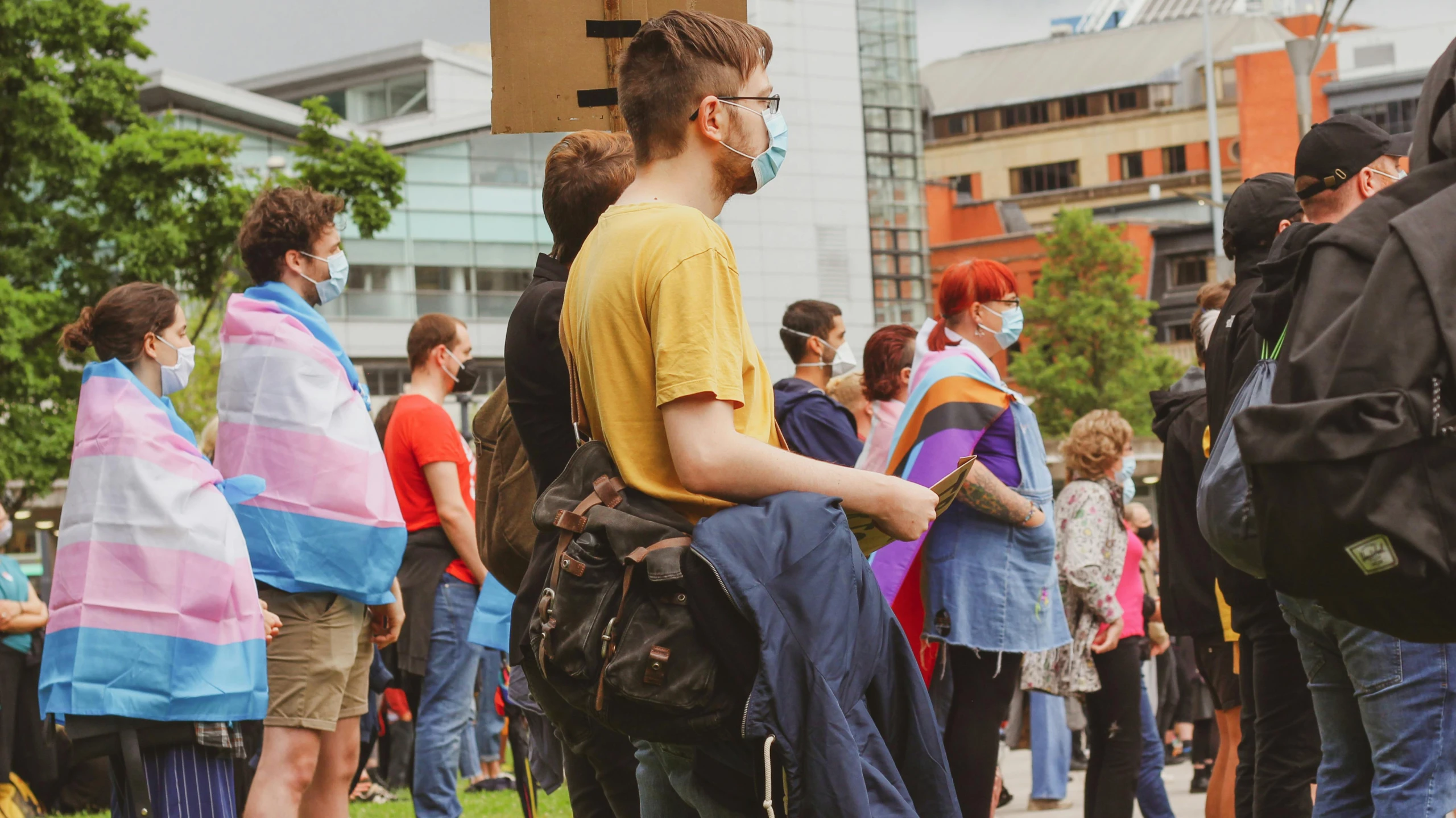 a group of people standing on top of a lush green field, coventry city centre, gay rights, a man wearing a backpack, waiting to strike