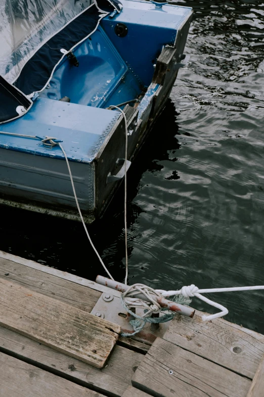 a blue boat sitting on top of a body of water, unsplash, auto-destructive art, floating power cables, sitting on a wooden dock, low quality photo, grey