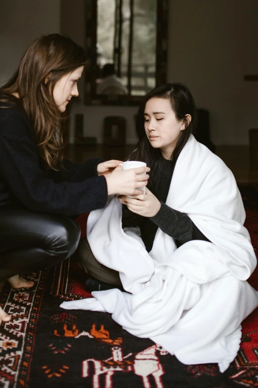 a couple of women sitting on top of a rug, trending on pexels, sick with a cold, wearing robe, with a white mug, asian female