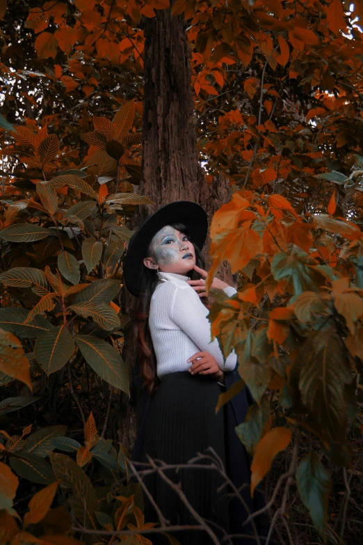 a woman in a witch costume standing next to a tree, an album cover, by reyna rochin, pexels contest winner, mime, fall colors, ☁🌪🌙👩🏾, photo of the girl