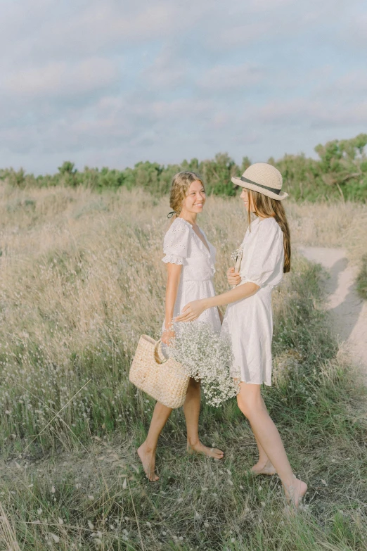 a couple of women standing next to each other in a field, happening, light cream and white colors, walking, unsplash photo contest winner, having a picnic