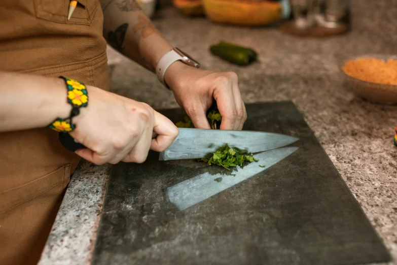 a close up of a person cutting vegetables on a cutting board, by Jessie Algie, a folding knife, slate, as chefs inside cthulhu, herbs