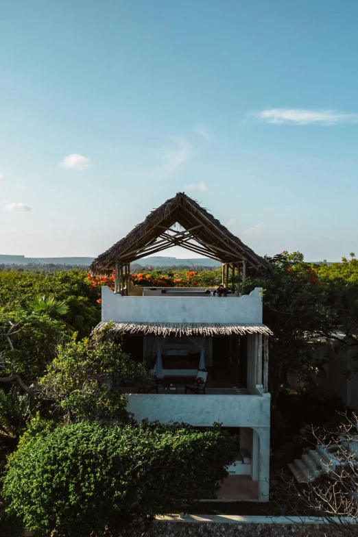 a house sitting on top of a lush green hillside, hurufiyya, in a beachfront environment, rooftop, afar, tropical vibe