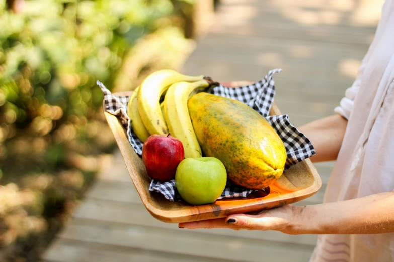 a close up of a person holding a tray of fruit, on a wooden plate, lush surroundings, high quality product image”, banana