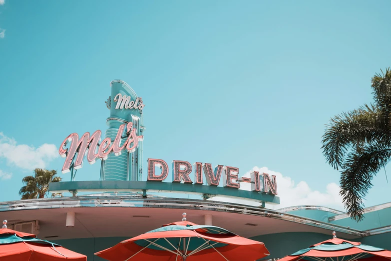 a number of umbrellas in front of a building, a colorized photo, by Ryan Pancoast, pexels contest winner, retrofuturism, drive in movie theater, neon sign, pink white turquoise, at california adventure