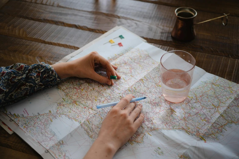 a person sitting at a table with a map and a glass of water, by Jessie Algie, pexels contest winner, holding pencil, road trip, tabletop gaming, national geographics