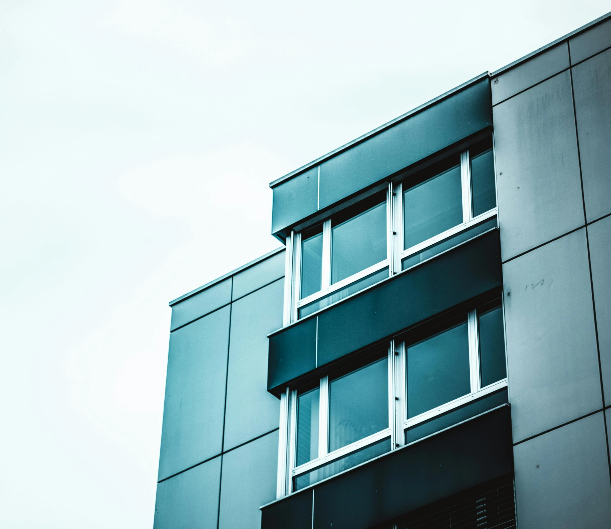 a tall building with windows on a cloudy day, a photo, unsplash, modernism, iron cladding, ten flats, teal aesthetic, over-the-shoulder shot