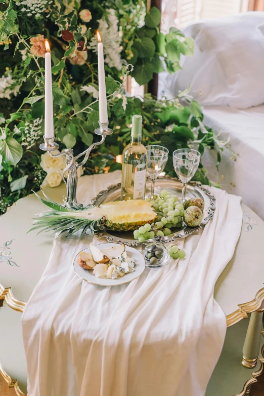 a table that has a bunch of candles on it, inspired by Konstantin Somov, trending on unsplash, rococo, wearing silver silk robe, eating a cheese platter, white bed, entwined in vines and nature