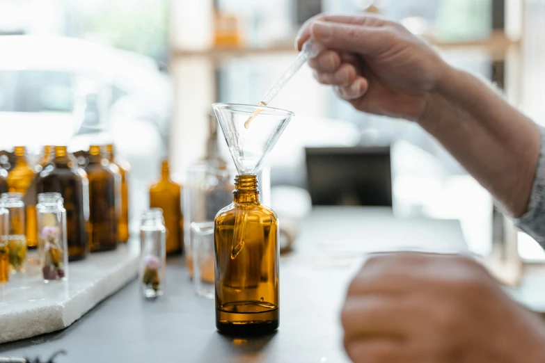 a person pouring a liquid into a glass bottle, by Adam Pijnacker, trending on pexels, apothecary, manuka, in a lab, brown