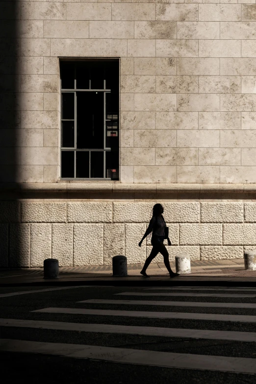 a person walking across a street next to a building, pexels contest winner, postminimalism, back light, madrid, girl running, deep shadow