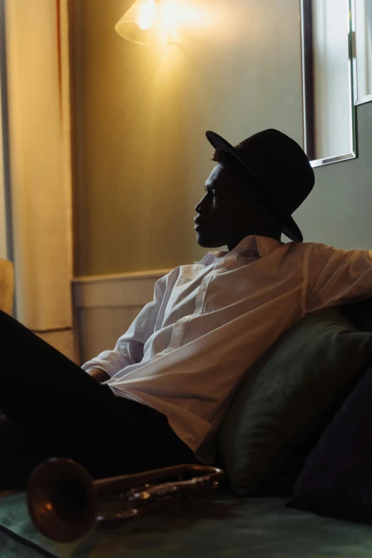 a man sitting on a couch with a trumpet, by Richmond Barthé, unsplash, visual art, androgynous person, with hat, dark skinned, contemplating existence