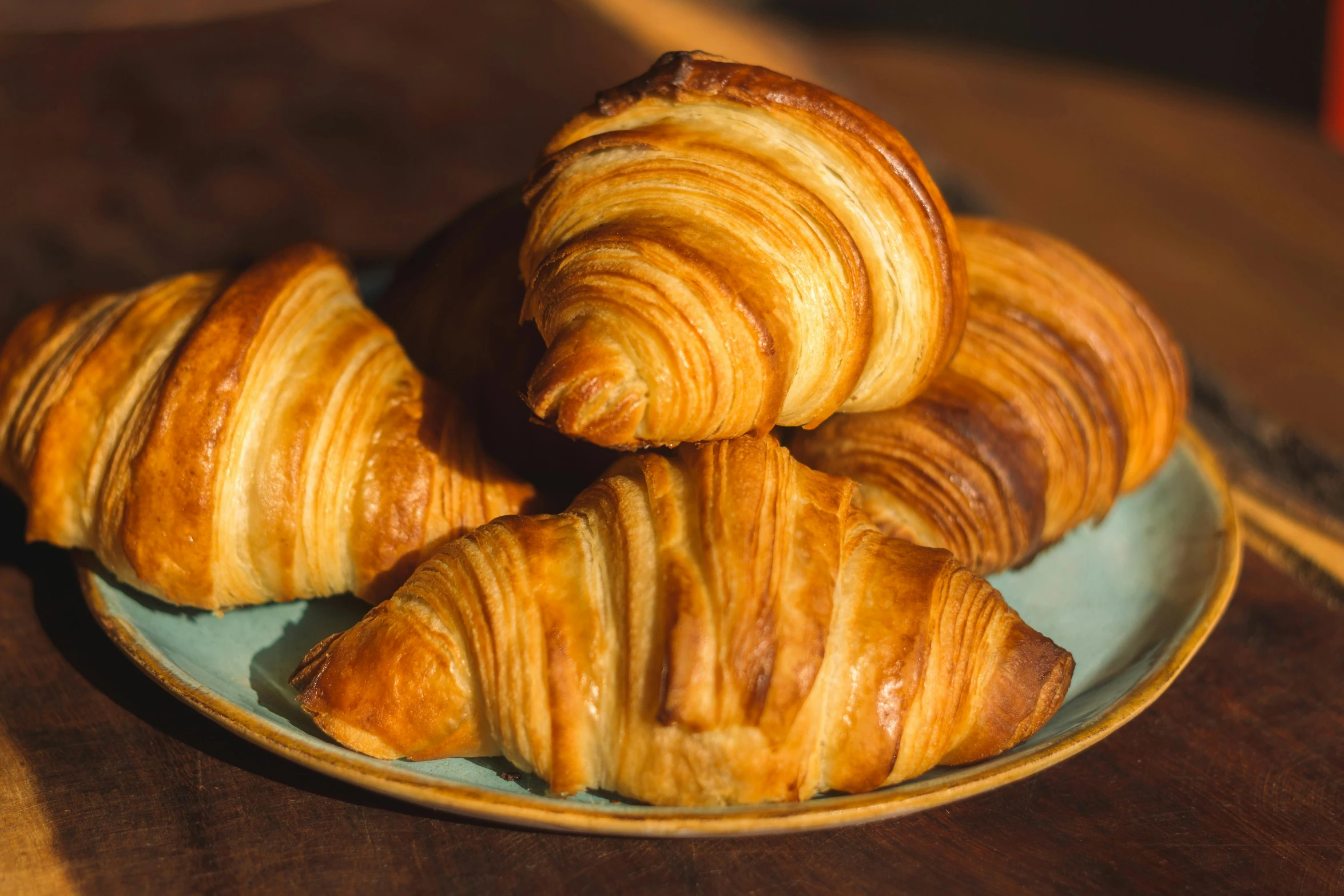 a blue plate topped with croissants on top of a wooden table, by Tom Bonson, unsplash, fan favorite, a pair of ribbed, chilean, bakery