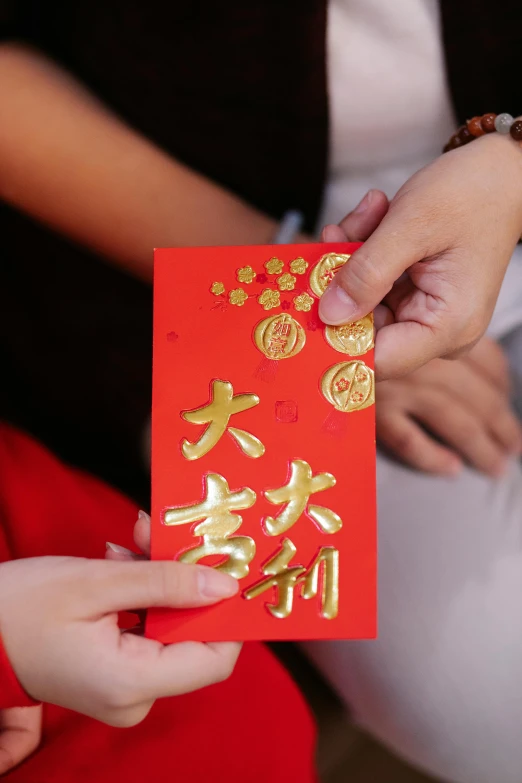 a close up of a person holding a red envelope, golden chinese text, kids, woman holding another woman, hands