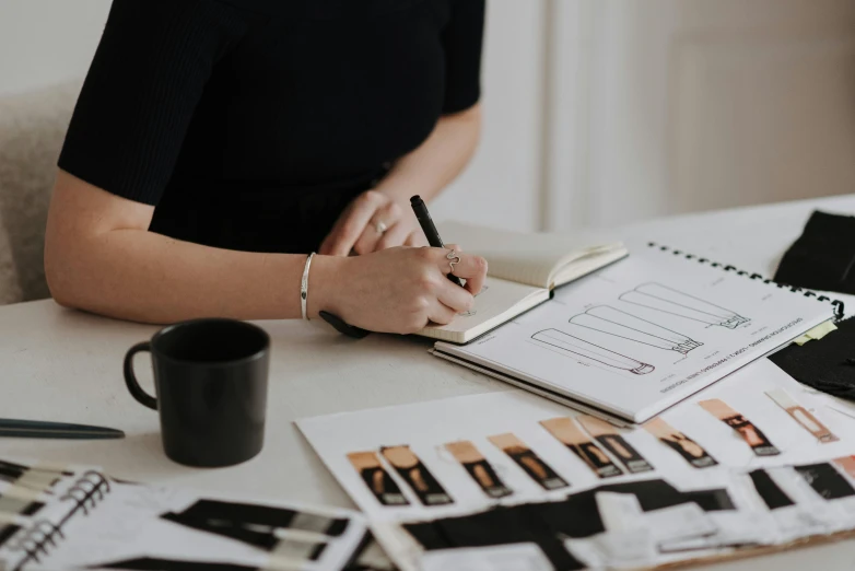 a woman sitting at a table writing in a notebook, a charcoal drawing, by Emma Andijewska, pexels contest winner, knolling, product design concept, wearing black modern clothes, charts