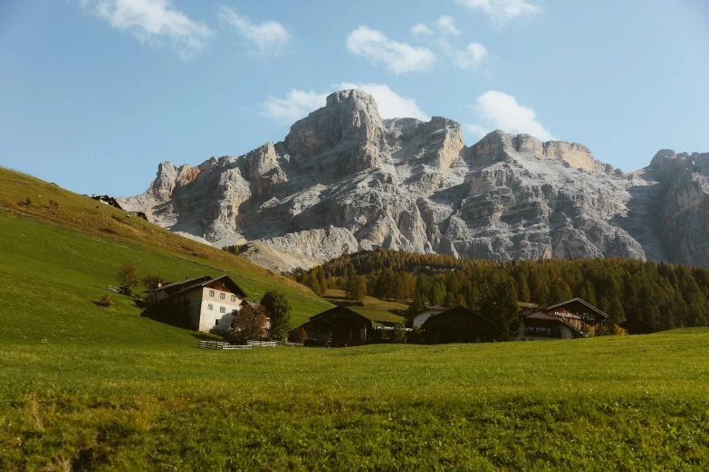 a group of houses sitting on top of a lush green hillside, an album cover, by Peter Churcher, pexels contest winner, renaissance, dolomites in background, grazing, youtube thumbnail, icy mountains in the background