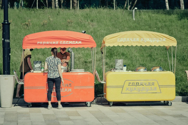 a couple of people standing next to a food cart, unsplash, socialist realism, yellow and orange color scheme, 000 — википедия, cardboard, square