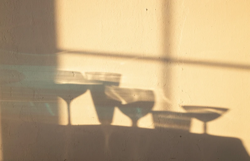 three wine glasses sitting on a table in front of a window, inspired by Elsa Bleda, light and space, casting long shadows, abstracted, 33mm photo, sunfaded