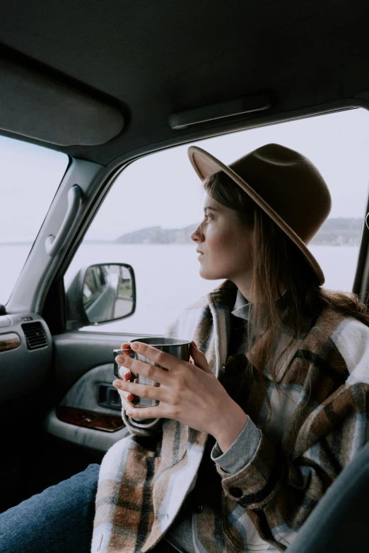 a woman sitting in a car with a cup of coffee, by Jessie Algie, happening, wearing wool hat, coast, square, high quality upload