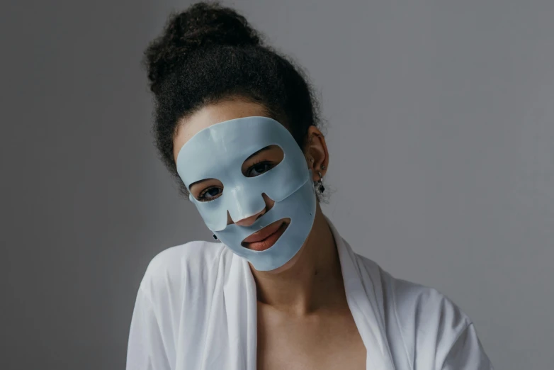 a woman with a blue mask on her face, product shot, grey mist, pastel blue, one single mask