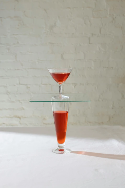 a glass filled with liquid sitting on top of a table, inspired by Méret Oppenheim, renaissance, red, tall, cone, balanced