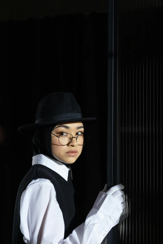 a man in a black hat and white shirt, an album cover, inspired by Yukihiko Yasuda, unsplash, hijab, fashion show photo, girl with glasses, photographed for reuters