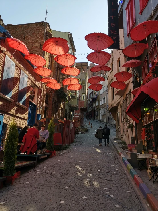 people walk down a cobblestone street lined with umbrellas, pexels contest winner, art nouveau, 'the red citadel, turkish and russian, back alley, slide show