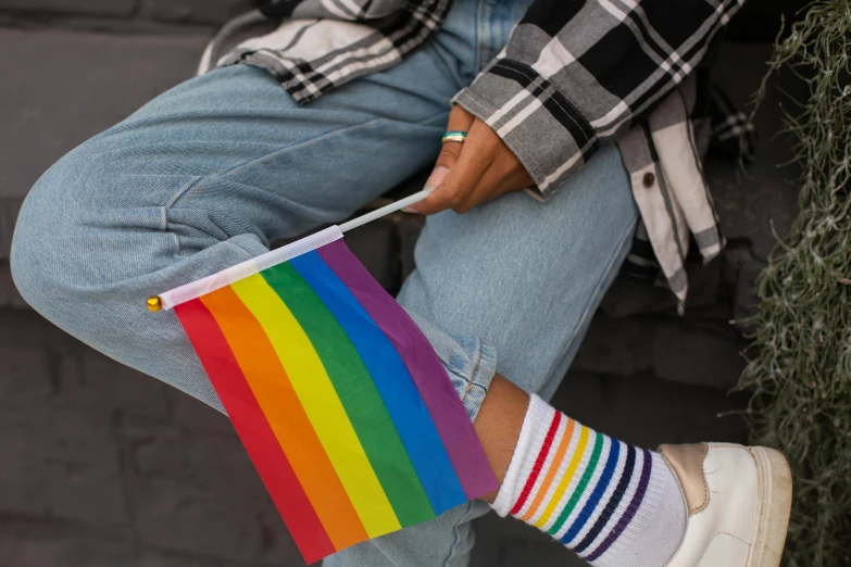 a person sitting down holding a rainbow flag, trending on pexels, striped socks, holding a white flag, male teenager, patterned