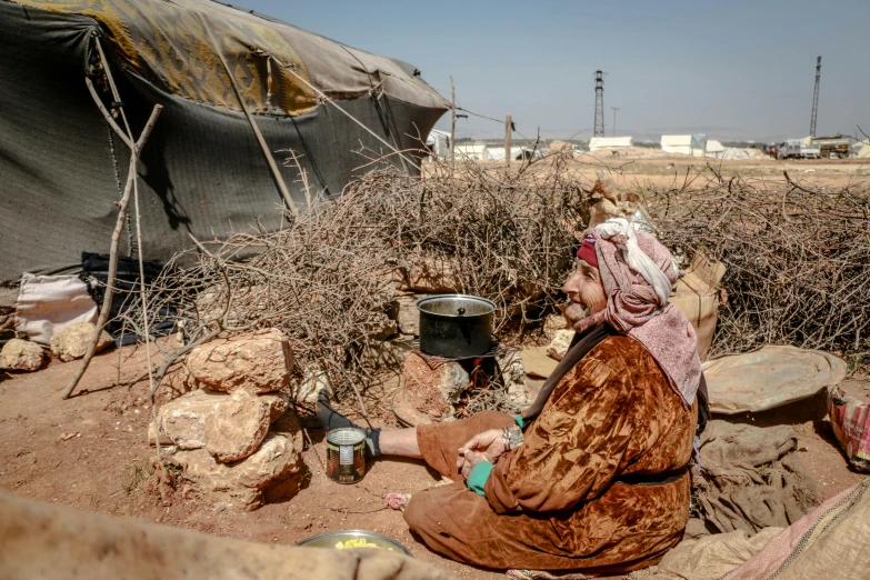 a woman sitting on the ground in front of a tent, dau-al-set, makeshift houses, profile image, malnourished, high resolution photo