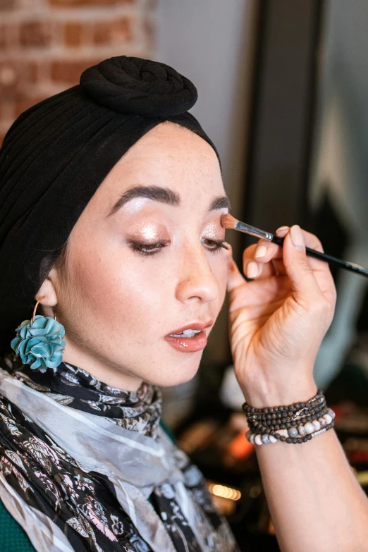 a woman is doing makeup in front of a mirror, by Julia Pishtar, hurufiyya, arabian nights inspired, smooth blending, complimentary eyeliner, muslim
