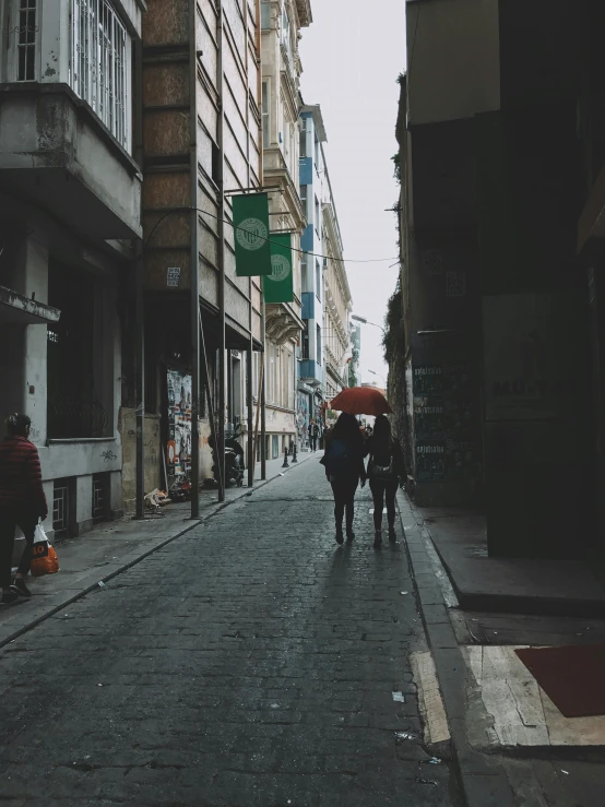 a group of people walking down a street next to tall buildings, a picture, inspired by Elsa Bleda, renaissance, single person with umbrella, istanbul, low quality photo, standing in an alleyway