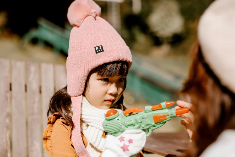 a little girl is playing with a toy gun, pexels contest winner, wearing beanie, heian, pink iconic character, with a kid