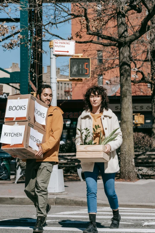 a man and a woman carrying boxes across the street, lush brooklyn urban landscaping, avan jogia angel, promo image, filled with books