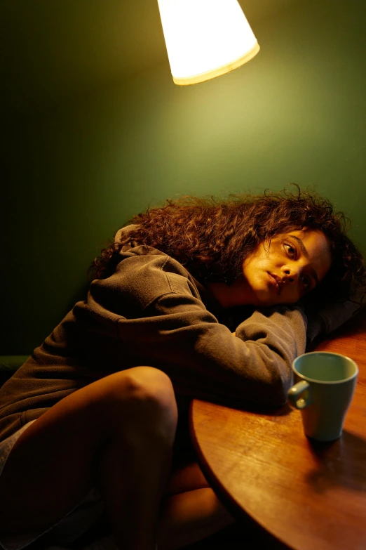 a woman sitting at a table with a cup of coffee, inspired by Nan Goldin, renaissance, curly dark hair, exhausted, promotional image, mixed-race woman