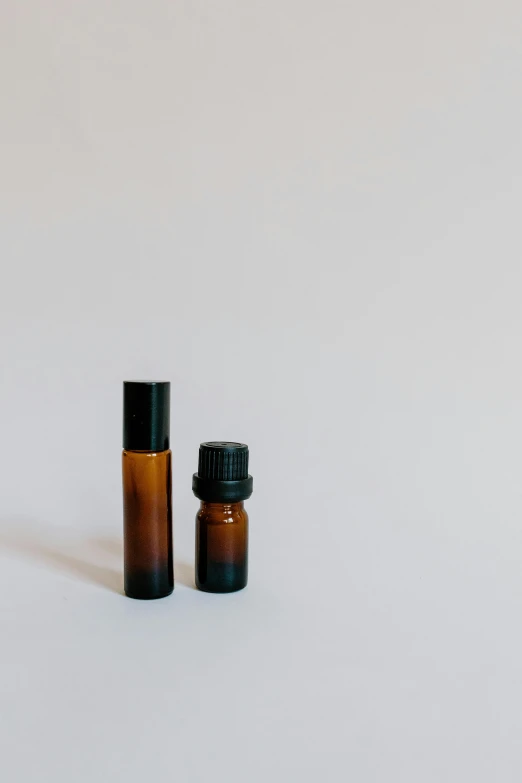 a bottle of essential oil next to a small bottle of essential oil, unsplash, plain background, brown, 1 9 9 9, 1 6 x 1 6