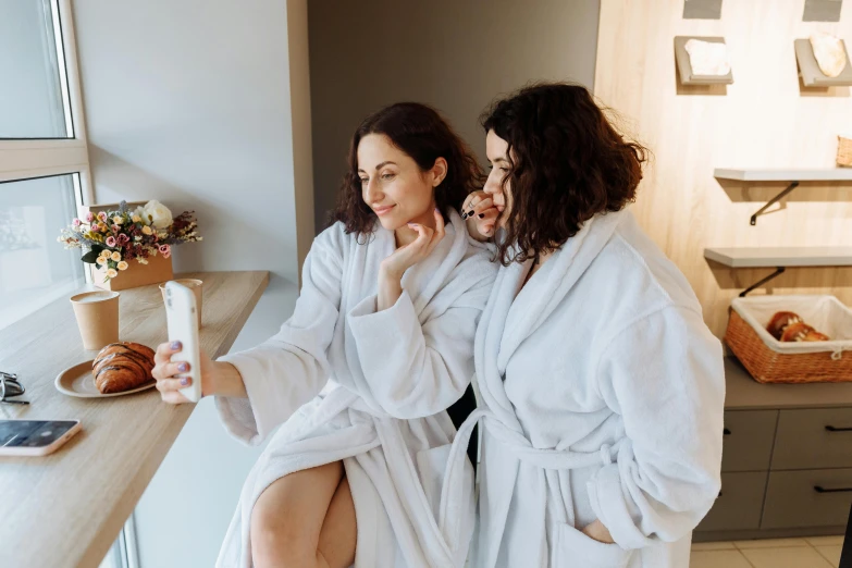 a couple of women sitting next to each other on a counter, by Emma Andijewska, pexels contest winner, happening, bathrobe, taking a selfie, spa, profile image