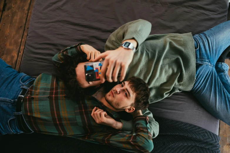 a man laying on top of a bed next to a woman, a polaroid photo, trending on pexels, two men hugging, looking at his phone, bowater charlie and brom gerald, brunette boy and redhead boy