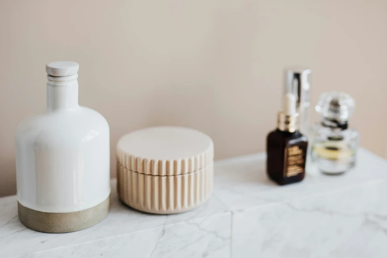 a couple of bottles sitting on top of a counter, a still life, trending on pexels, minimalism, cream white background, bath, jar on a shelf, on a marble pedestal