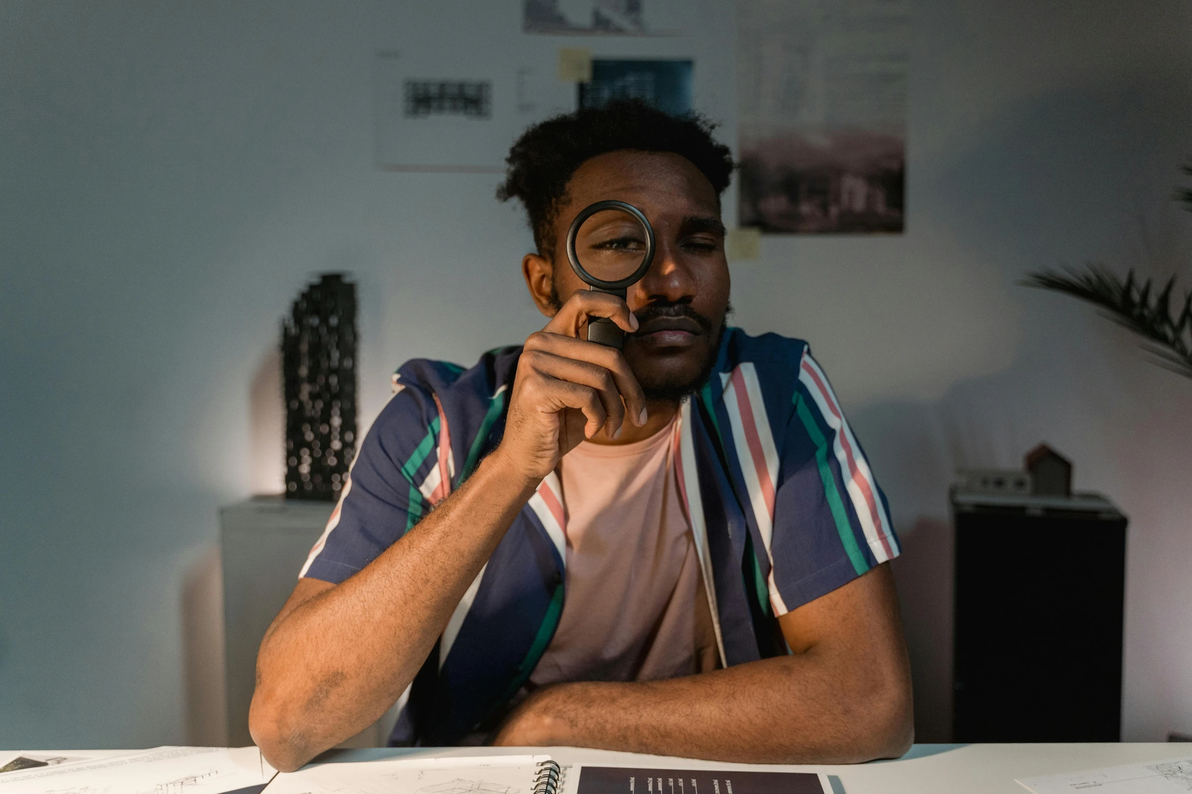 a man sitting at a table looking through a magnifying glass, a character portrait, pexels contest winner, black man, studious, low quality photo, avatar image