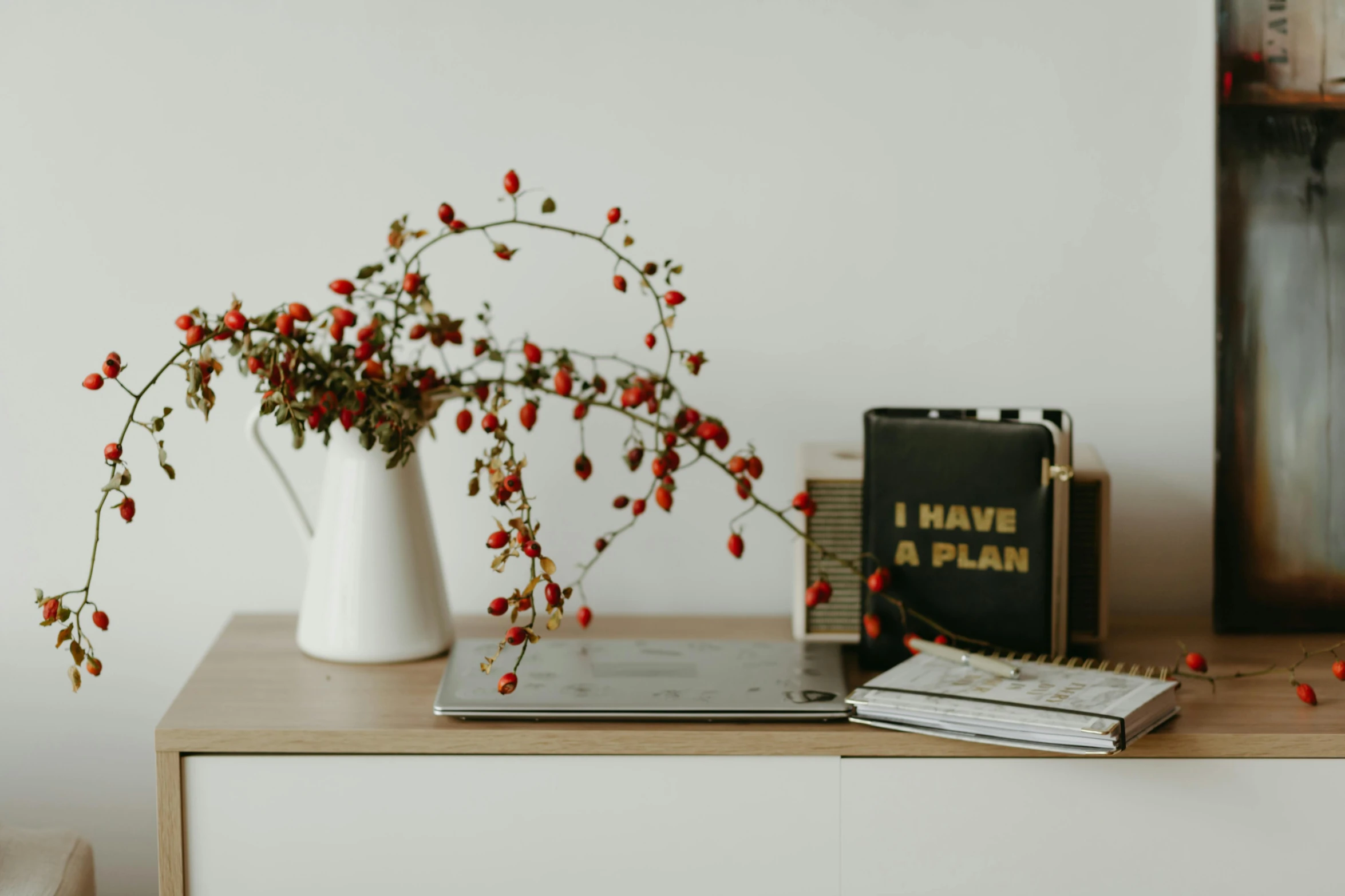 a white vase sitting on top of a wooden table, a picture, by Emma Andijewska, unsplash, gold and red accents, beautiful plans, berries, home office