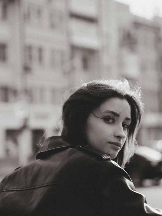 a black and white photo of a woman sitting on a bench, a black and white photo, by Lucia Peka, pexels contest winner, photorealism, wearing leather jacket, young middle eastern woman, standing in a city street, russian girlfriend