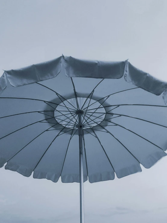 a white umbrella sitting on top of a sandy beach, blue / grey background, solid grey, picton blue, impactful