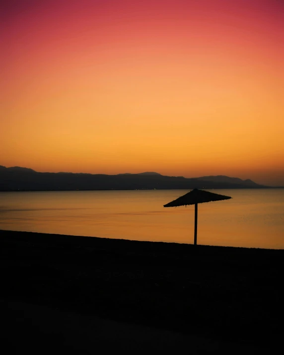 an umbrella sitting on top of a beach next to the ocean, by Alexis Grimou, sunset in the distance, profile image, the dead sea, colorful image