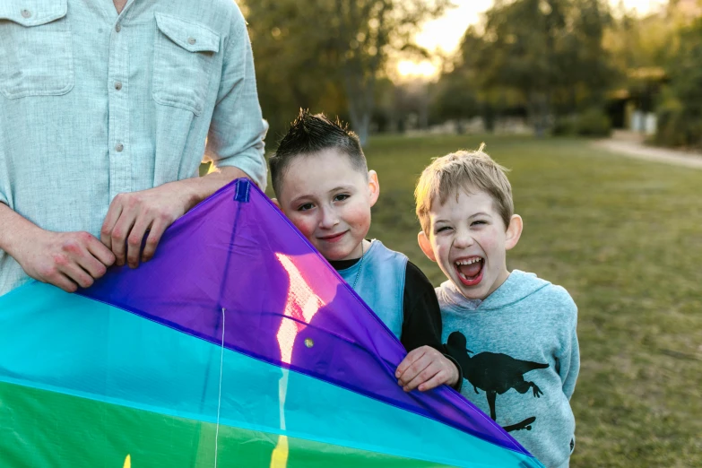 a man standing next to two boys holding a kite, pexels contest winner, lachlan bailey, avatar image, warm and joyful atmosphere, close - up photo