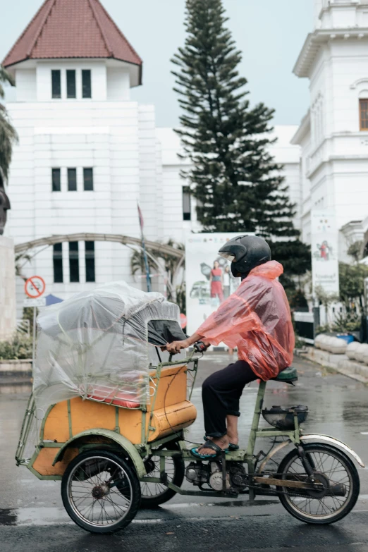 a person riding a bike with a cart on the back, by Yosa Buson, unsplash, visual art, white marble buildings, plastic wrap, indonesia, bad weather