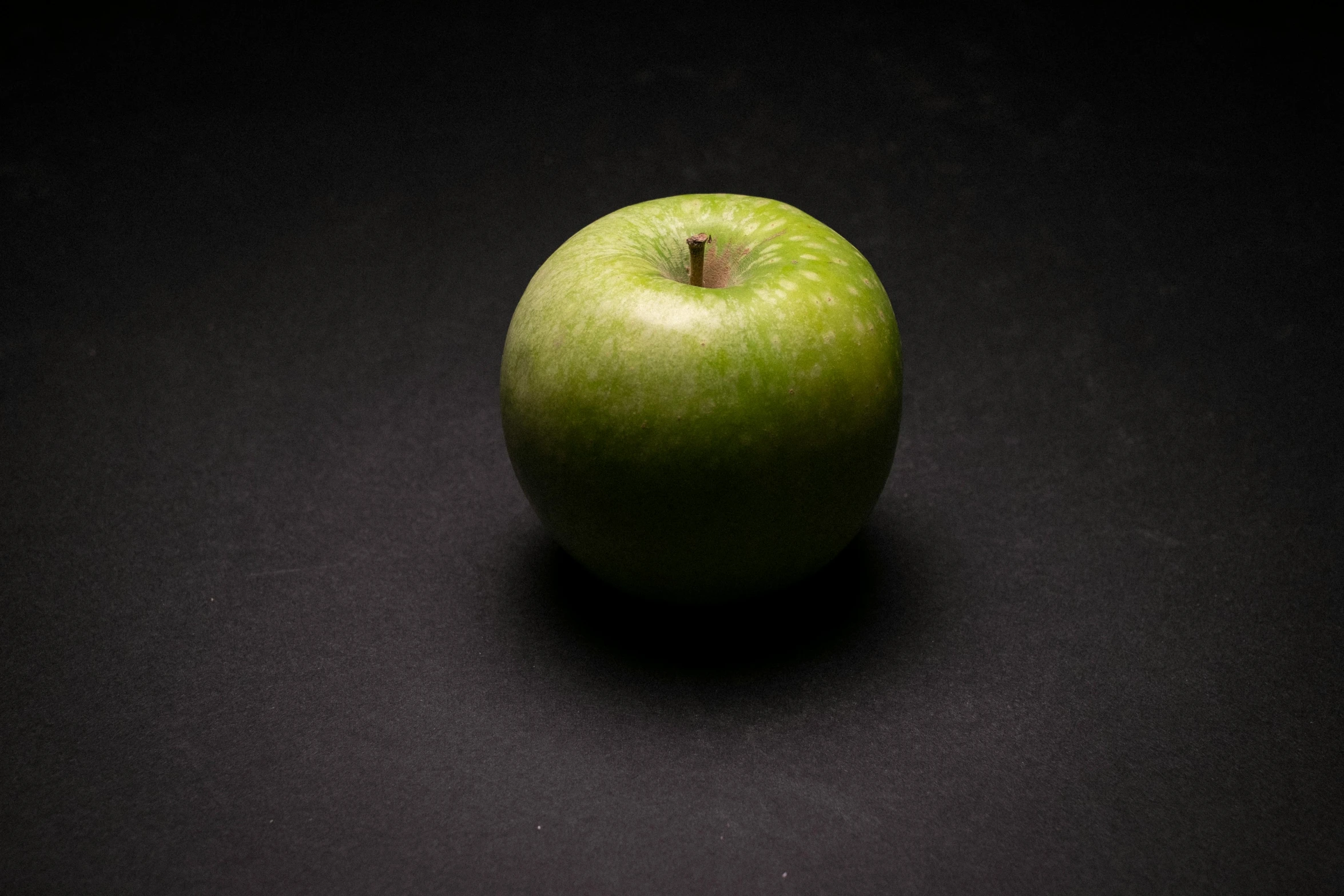 a green apple sitting on top of a black surface