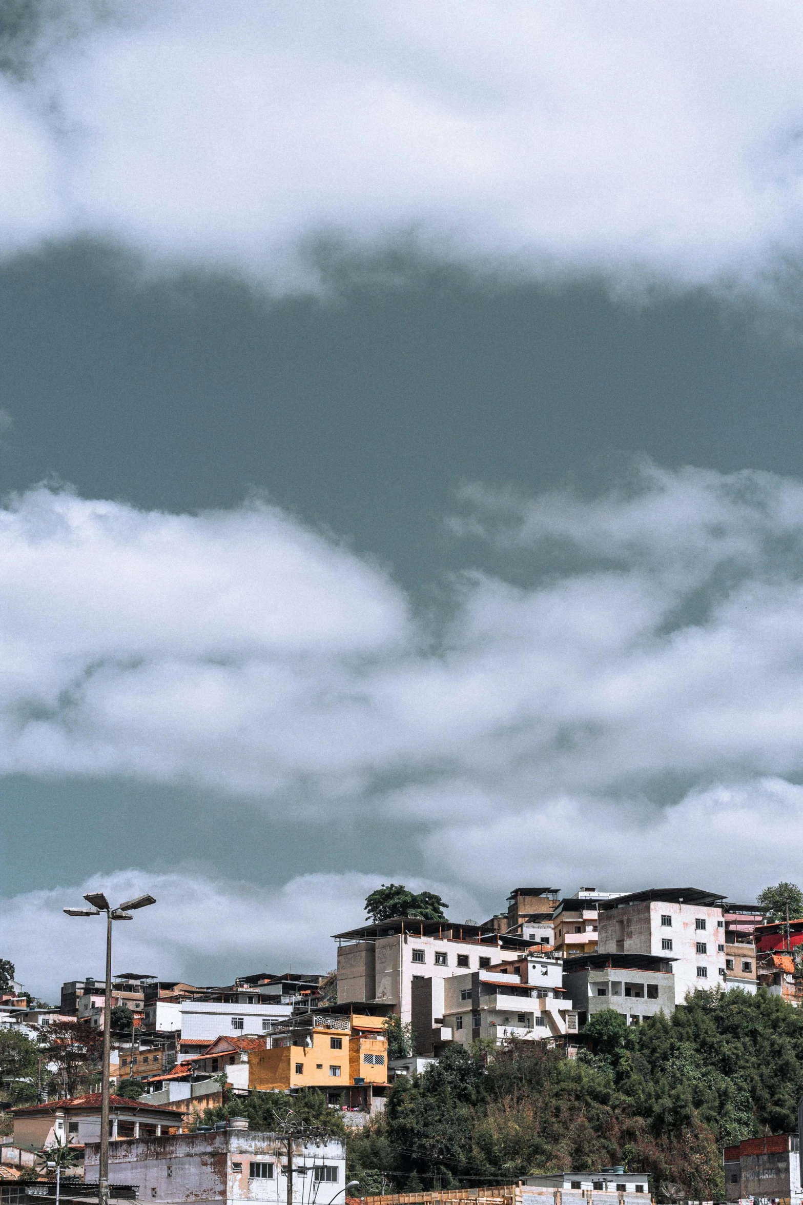 a group of buildings sitting on top of a hill, by Nadir Afonso, pexels contest winner, quito school, round clouds, location ( favela _ wall ), panorama view of the sky, square